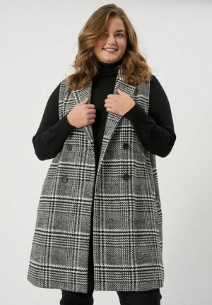 Schwarz-weißes karriertes Weste mit doppelreihigem Design, großen Knöpfen und taillierter Schnitt. Trägt man über einem schwarzen Rollkragenpullover.