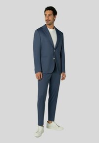 Marineblauer Blazer und passende slim-fit Hose aus strukturiertem Stoff, kombiniert mit einem weißen T-Shirt und weißen Sneakern.