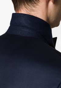 Kołnierz granatowej marynarki widziany z tyłu, wykonany z teksturowanej tkaniny o gładkim wykończeniu oraz subtelnych detalach przeszyć.