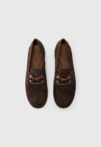 Chaussures en daim marron avec une forme arrondie, dotées d'œillets et de lacets dorés, ainsi que d'une surface texturée. Inscription « super doux » visible à l'intérieur.