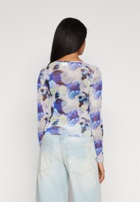 Långärmad topp i genomskinligt material med ett blått och lavendelfärgat blommönster, rund halsringning och en figurnära silhuett. Kombineras med ljus denim.