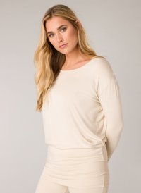 Beige Langarmshirt aus weichem Material, mit rundem Ausschnitt, lockerer Passform und Raffung am Saum. Glatte Textur über das gesamte Shirt.