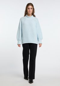 Light blue knitted sweater with a high neckline, dropped shoulders, and ribbed cuffs. Paired with black straight-leg pants and black boots.