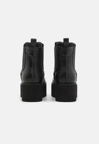 Botas negras de tobillo con un acabado texturizado, que cuentan con un forro de piel sintética y tacón bloque. La vista trasera muestra el logotipo y un diseño elegante.
