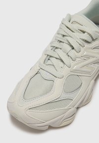 Baskets vert clair avec une tige en maille texturée et en cuir lisse, bout rond et semelle épaisse légèrement courbée. Les lacets sont gris clair.