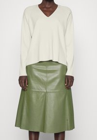 Krämfärgad ribbad stickad v-ringad tröja kombinerad med en olivgrön läder midi-kjol med vid silhuett och sömdetaljer.