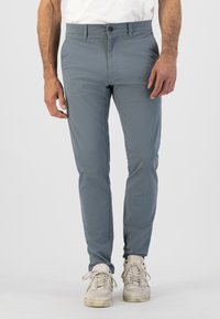 Pantalon gris slim-fit en tissu léger ; doté d'une fermeture à bouton, de poches avant et d'une texture lisse. Associé à des baskets claires.