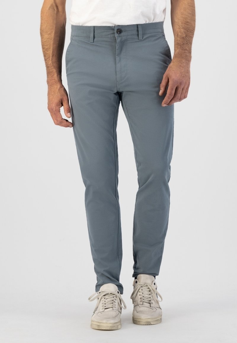 Pantalon gris slim-fit en tissu léger ; doté d'une fermeture à bouton, de poches avant et d'une texture lisse. Associé à des baskets claires.