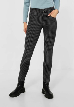 Pantalons noirs à motifs avec une coupe slim, présentant un design géométrique et une fermeture à bouton à l'avant. Associés à des bottines noires.