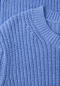 Gros plan sur le tissu d'un pull tricoté bleu clair montrant un col côtelé et un motif de point texturé.