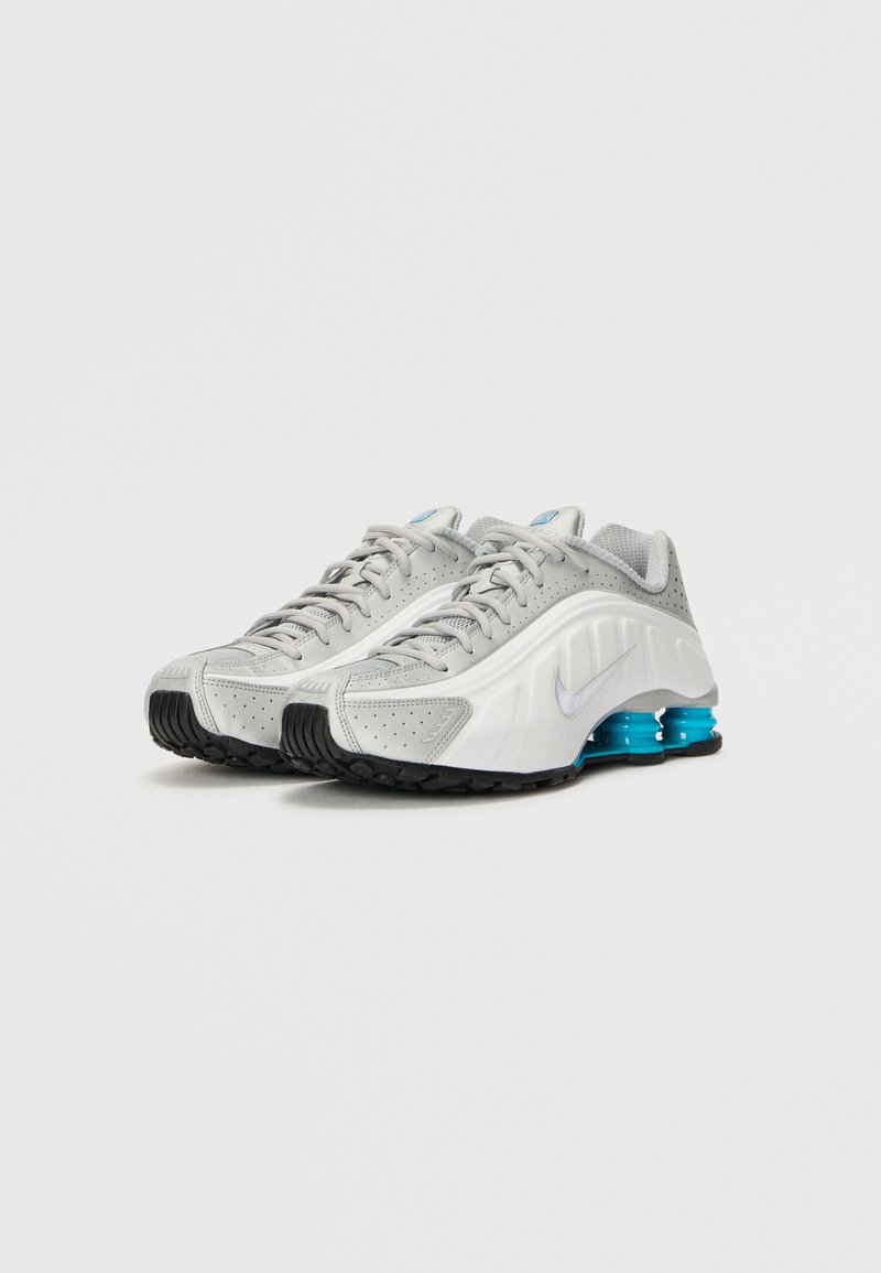Zapatillas deportivas grises con una suela blanca y azul, que cuentan con un upper texturizado, paneles de malla y un logo de marca prominente.