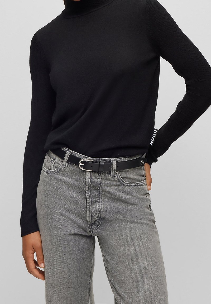 Un pull noir à col roulé côtelé associé à un jean en denim gris clair et une fine ceinture noire avec une boucle en argent.