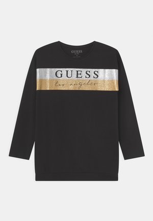 Sort langærmet skjorte med sølv- og guldfarvede metalliske vandrette striber over brystet, med teksten "GUESS" og "los angeles".