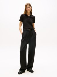 Polo noir avec un col boutonné, associé à un pantalon large noir et des mocassins noirs. Design simple et texture lisse.