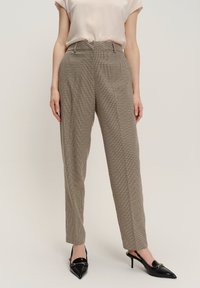 Pantaloni sartoriali a quadri beige con vita alta, gamba dritta e pieghe sottili. Abbinati a tacchi neri a punta.