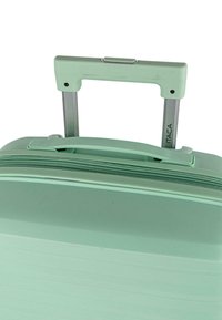 Maleta rígida verde menta con asa telescópica extendida y cierre de cremallera, etiquetada "ITACA" en la barra metálica del asa.