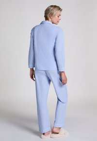 Ljusblå randig pyjamas med långa ärmar, uppvikta byxor och krage, tillverkad av mjukt tyg. Krämfärgade, fluffiga tofflor.