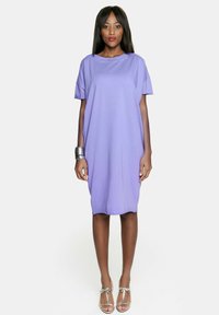 Fioletowa sukienka z krótkim r ękawem o luźnym kroju, gładkiej fakturze i okrągłym dekolcie. Noszona z srebrnymi bransoletkami i sandałami.