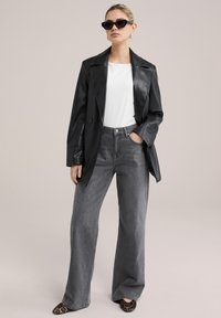 Svart läderblazer, vit topp, grå vida jeans och loafers med djurtryck. Tillbehören inkluderar svarta solglasögon och silverfärgade hoops.