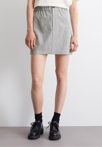Falda gris a rayas con una cinturilla elástica, corte recto y diseño hasta la rodilla. Combinada con zapatos negros de cordones y calcetines.