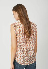 Top senza maniche in tessuto leggero con base crema e motivo geometrico arancione e rosa. Presenta dettagli arricciati sulle spalle e un orlo arrotondato.