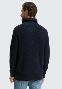 Navy-blauer Strickpullover mit hohem Kragen, der Farbspritzer in verschiedenen Farben aufweist. Die Textur ist gerippt, mit langen Ärmeln und einer lockeren Passform.