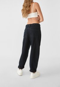 Tummat farkut korkealla vyötäröllä, rento istuvuus, käännetyt lahkeensuut ja kaksi takataskua, yhdistettynä valkoisiin tennareihin ja istuvaan lyhytpaitaiseen yläosaan.