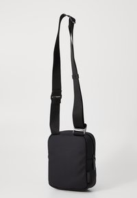 Borsa a tracolla nera con una finitura liscia e opaca, dotata di spallacci regolabili e forma rettangolare con un compartimento con zip.