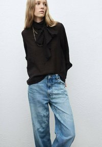 Blusa negra de manga larga con cuello de lazo, combinada con jeans de corte holgado en un tono azul claro, que presentan un desvanecimiento sutil y un diseño relajado.
