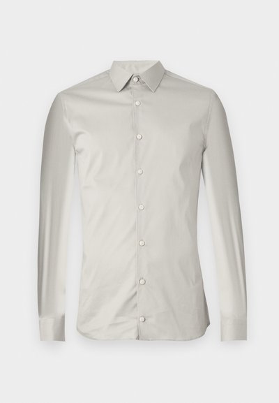Svetlo siva majica s dolgimi rokavi, izdelana iz gladkega blaga. Ima usnjeno ovratnico, sprednje gumbe in krojen fit s minimalnim dizajnom.