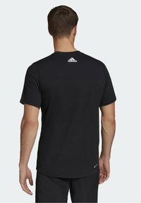 Musta puuvillapaita, jossa on lyhyet hihat ja pyöreä kaula-aukko. Takana, kauluksen lähellä, on valkoinen Adidas-logo.