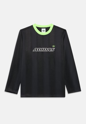Czarna koszulka Adidas z długim rękawem, subtelne pionowe paski, neonowo zielony kołnierz, biały napis z logo Adidas oraz mała zielona emblemat czterolistnej koniczyny na piersi.
