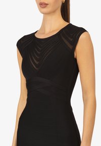 Zwart jurkje met een getailleerde lijfje, cap sleeves en horizontale gestreepte lagen. Soepele textuur met doorschijnende details op de schouders en de halsline.