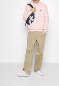 Felpa rosa con logo, pantaloni in corda beige, borsa a tracolla in camo bianco e nero e sneakers bianche con dettagli rosa.