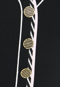 Maglione nero a maglia con tre bottoni dorati a righe, caratterizzato da linee verticali bianche e rosa lungo la parte anteriore. Tessuto morbido, design aderente.