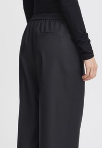 Zwarte wijde broek gemaakt van een gladde stof, met een elastische tailleband en een achterzak met een ton-sur-ton naaddetail.