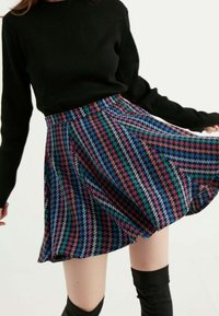 Sukně A-line z vlněné směsi s vícebarevným vzorem houndstooth, má přiléhavý pas a rozšířený lem, spárovaná s černým žebrovaným topem s dlouhým rukávem.