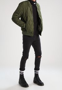 Zielona pikowana kurtka bomberska z prążkowanym kołnierzem, w połączeniu z czarnymi, podartymi dżinsami i czarnymi botkami na sznurowadła. Charakteryzuje się kontrastowymi białymi skarpetami w paski.