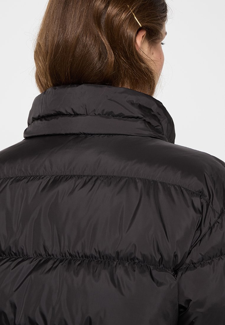 Schwarze Daunenjacke mit hohem Kragen und gestepptem Muster. Das Material wirkt glatt mit sichtbaren Nähten und einer leicht reflektierenden Textur.