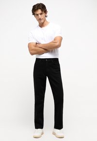 Jeans negros de corte recto, tela de mezcla de algodón, diseño de cinco bolsillos y un ligero desgaste. Combinados con una camiseta blanca sencilla y zapatillas blancas.