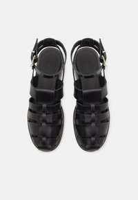 Μαύρα σανδάλια από δέρμα με πλεγμένο σχέδιο. Διαθέτουν ρυθμιζόμενες ταινίες στον αστράγαλο και επίπεδο πάτο. Λείο υφή, μινιμαλιστικό στυλ.