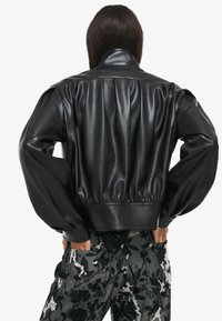 Černá bomber bunda z umělé kůže s cropped střihem, řaseným lemem a objemovými rukávy. Obsahuje klasický límec a hladkou texturu.