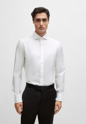 Weißes Hemd mit Kentkragen, langen Ärmeln und glatter Textur, kombiniert mit schwarzen Hosen.