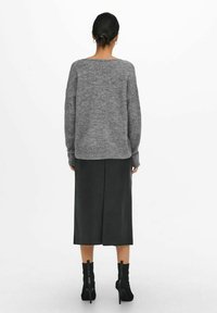 Grijze gebreide trui met een ontspannen pasvorm, gecombineerd met een zwarte leren midi-rok. Zwarte enkellaarsjes met ritssluiting maken de look compleet.