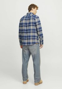 Flanellen blouse met een blauw en beige ruitpatroon, lange mouwen en een rugplooitje. G gedragen met lichtblauwe jeans en tan kleurige laarzen.