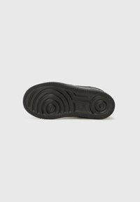 Svart gummisåle til sneakers med sirkulære mønstre, fremtredende spor og en teksturert finish. Har en synlig logo og hevede kanter.