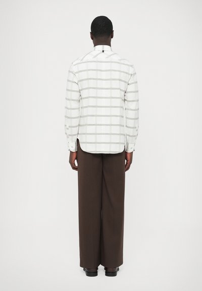 Wit geruit overhemd met grijze lijnen, voorzien van een puntkraag en knoopmanchetten. Gecombineerd met bruine broek met wijde pijpen en zwarte schoenen.