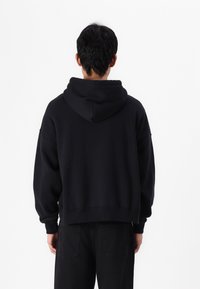 Sweatshirt preto com capuz, com um ajuste relaxado, apresentando um capuz espaçoso, punhos e barra canelados. A vista traseira mostra um design simples e minimalista.