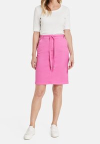 Vaaleanpunainen farkkuhame, jossa on vyötärölle solmittava nauha, polvipituinen muotoilu ja taskut. Yhdistetty valkoiseen lyhythihaiseen puseroon ja valkoisiin tennareihin.