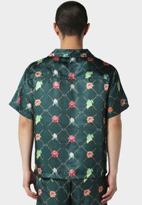 Camisa de manga corta con tejido de satén verde y un patrón floral en tonos rosas y verdes, acentuada con diseños de rasguño cruzado.